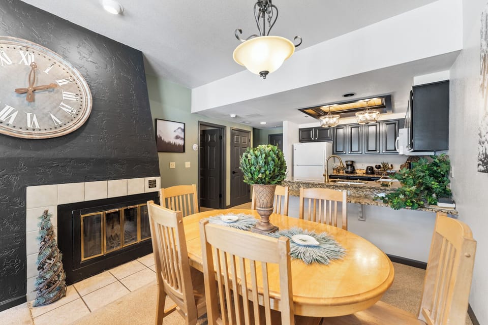 Your dining table awaits beneath warm lighting, with a cozy fireplace nearby and fully-equipped kitchen ready for meal preparation.