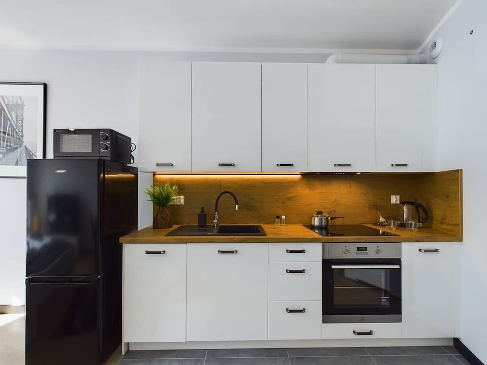 White modern cabinets, built-in oven, induction hob, fridge, and yellow backsplash with under-cabinet lighting.
