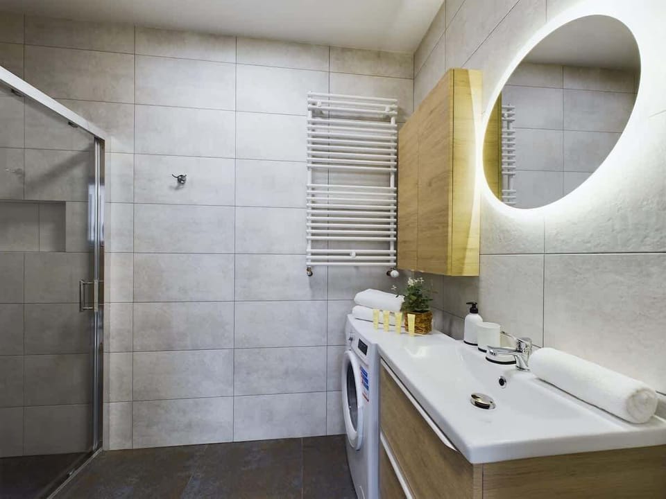 Modern sink with a large round mirror and wooden cabinetry.