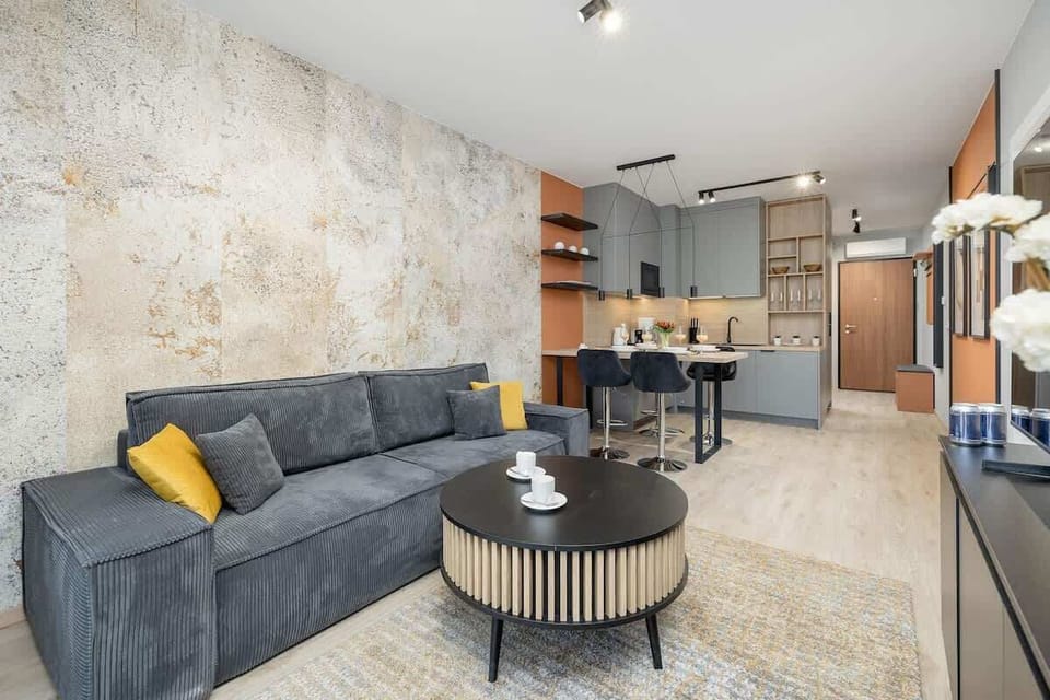 A bright living room with a gray sofa, coffee table, armchair, and large window with sheer curtains.