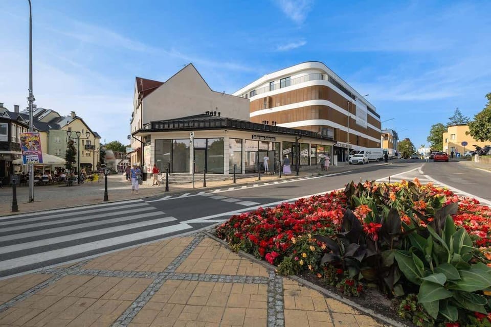 Scenic street with flowers, modern buildings, and clear blue sky.