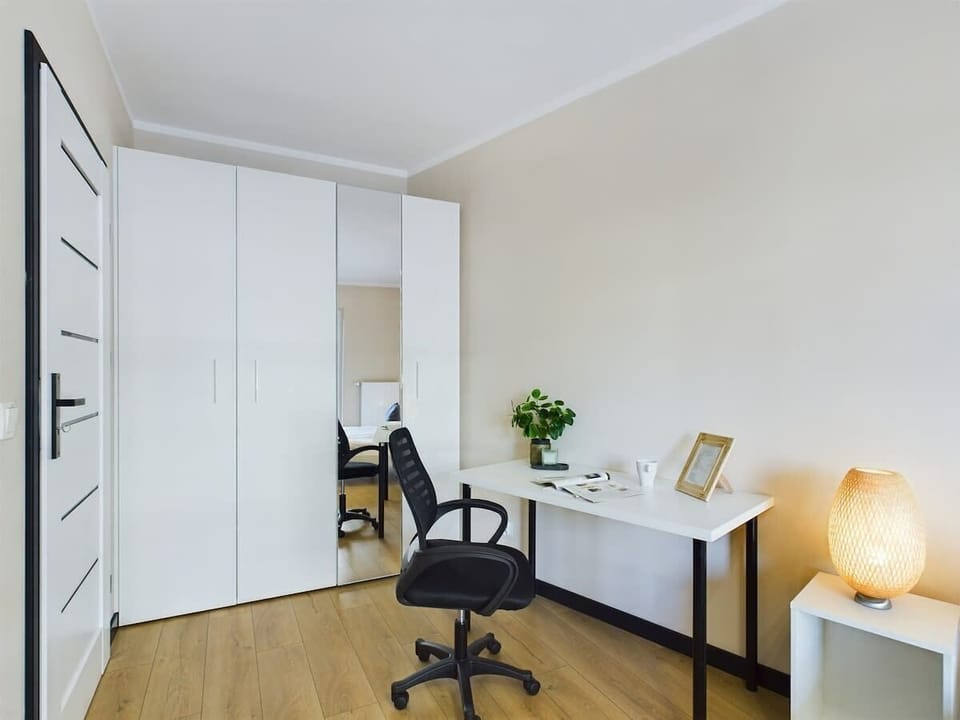 A bright bedroom with a desk, double bed, and wardrobe in white and wood tones.