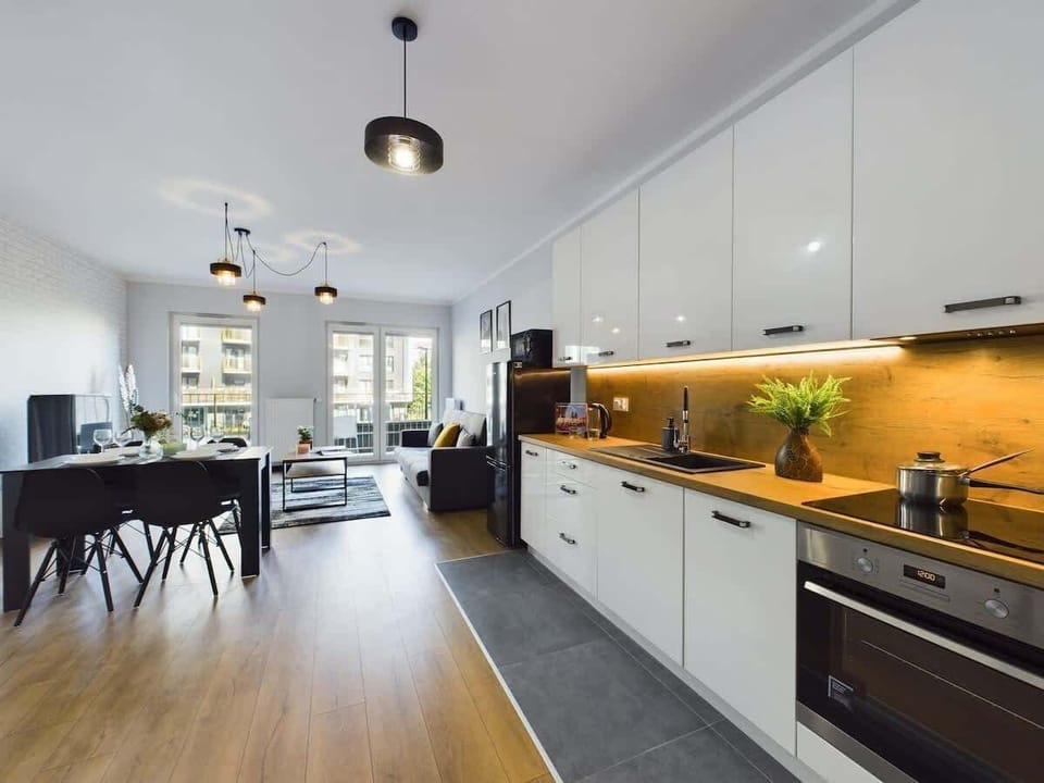 A sleek kitchen and dining area with a wooden floor, white cabinetry, and warm lighting.