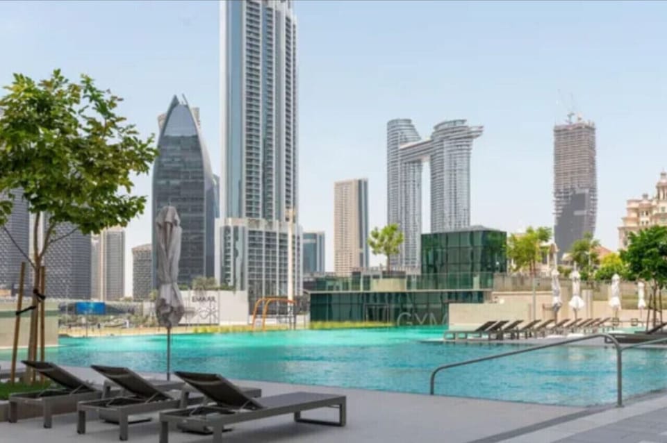 A luxurious pool area surrounded by sun loungers, with impressive views of nearby skyscrapers.