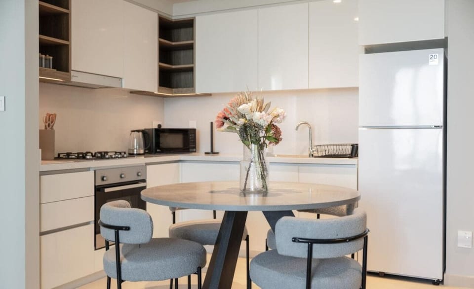 A modern, fully equipped kitchen with white cabinetry and a round dining table, perfect for home-cooked meals.