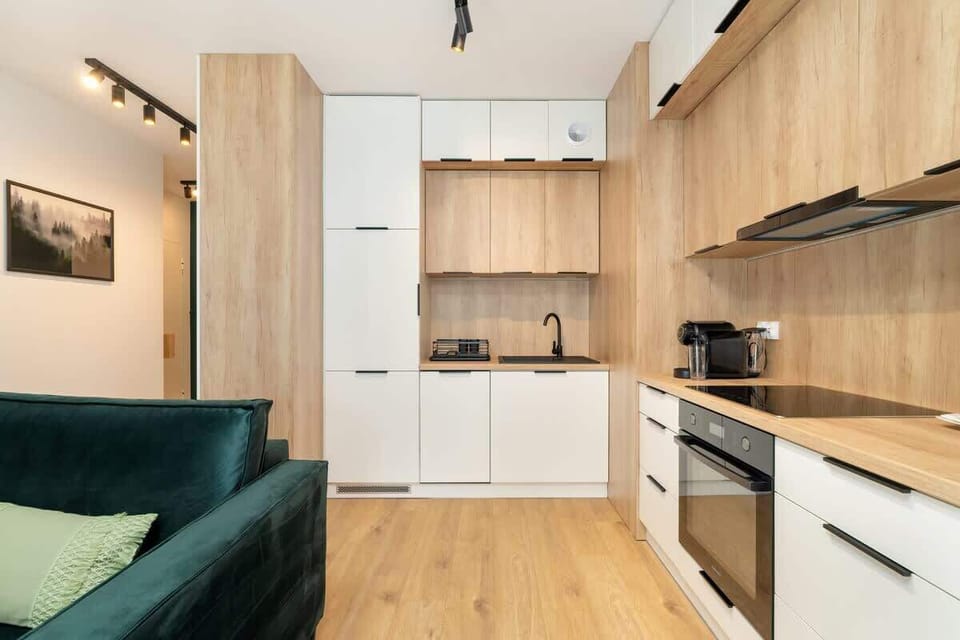 Kitchen designed with white and wooden cabinetry, black appliances, and discreet overhead lighting.
