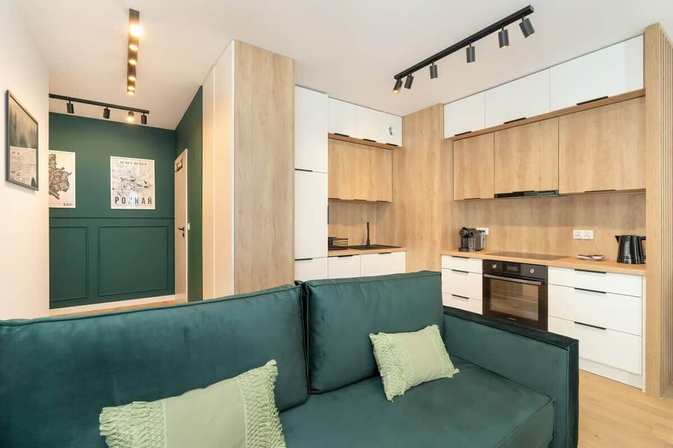 A stylish space featuring a green sofa, modern lighting, and a view of the open-plan kitchen with wood cabinetry.