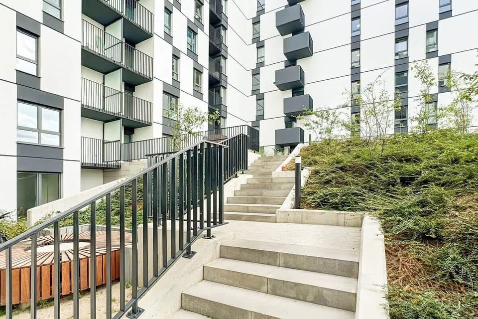 Building entrance surrounded by greenery and steps leading up to the modern residential complex.