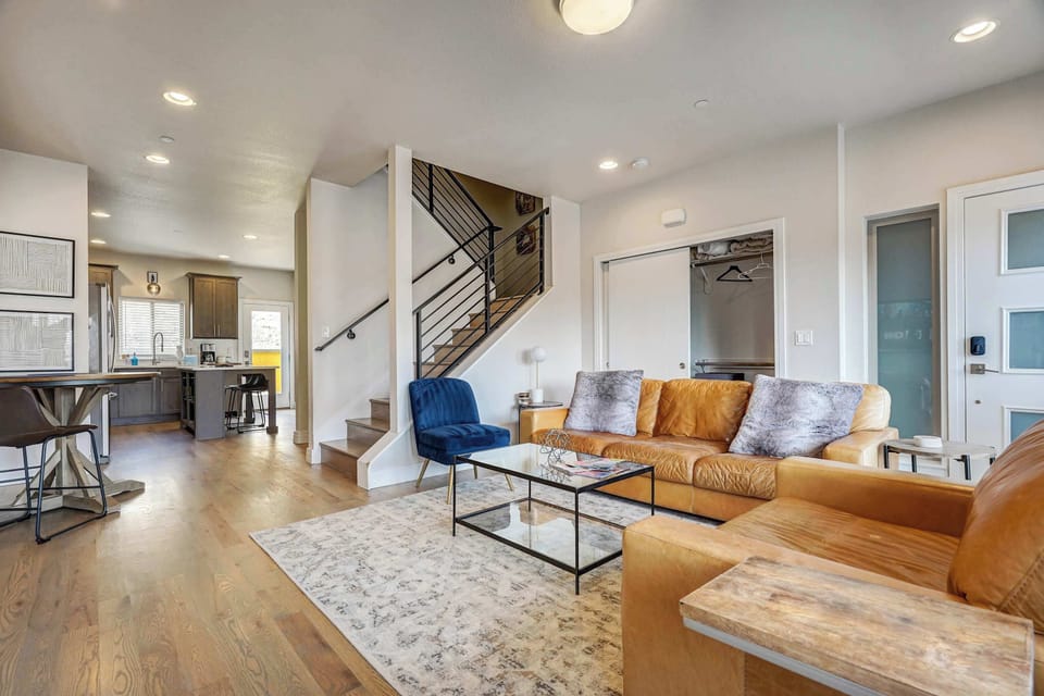 Open living area with layered seating, an area rug, and a dining space flowing together under tall ceilings. The layout encourages gathering, lounging, and easy movement, with warm textures and natural light tying the whole space together.