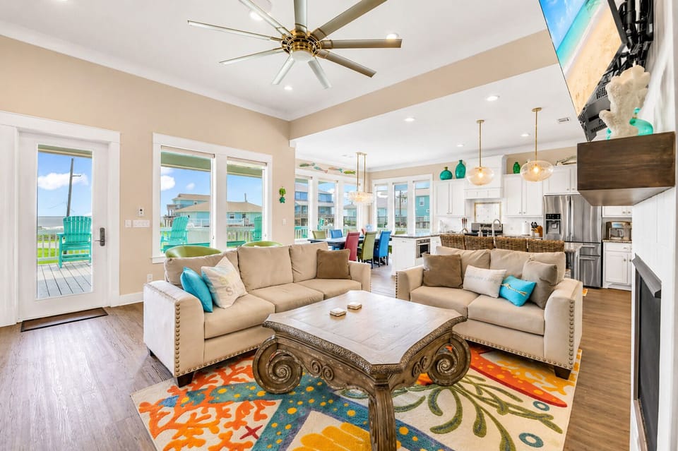 Coastal-style living room with large sectional, colorful rug, and open kitchen view