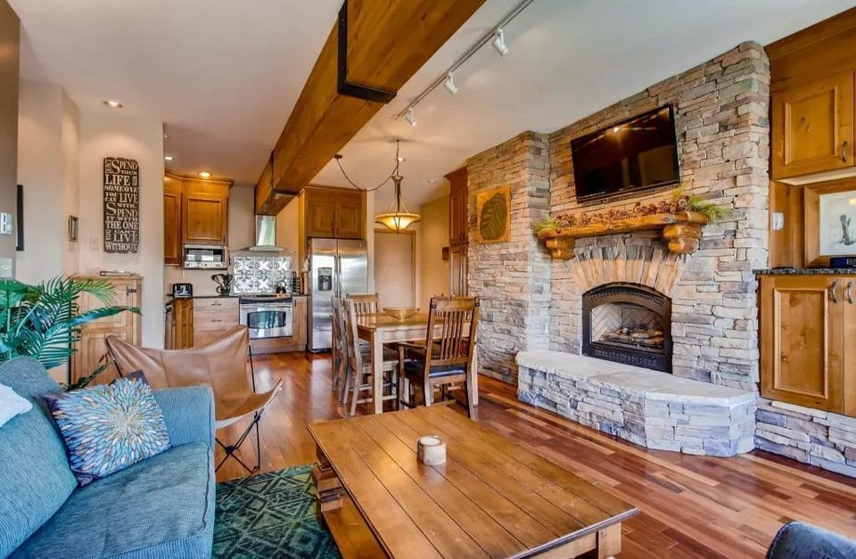 The spacious living area, adorned with cozy mountain decor and a stone fireplace, creates an inviting atmosphere perfect for relaxation after a day on the slopes.