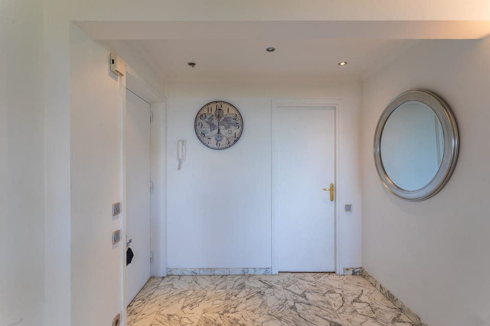 Elegant and bright entrance with marble flooring, minimalist decor featuring a round mirror and a wall clock.