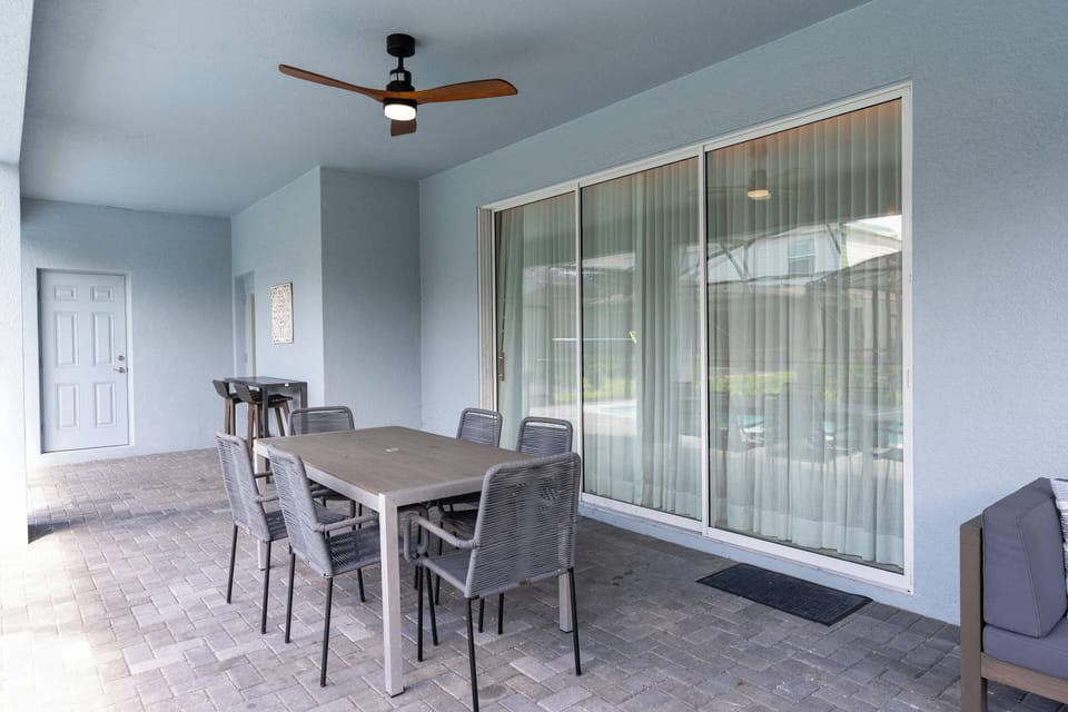 Step outside to a spacious patio featuring a stylish dining set and a refreshing ceiling fan, perfect for al fresco meals. The soft blue walls create a calming atmosphere, inviting you to relax and enjoy the view.