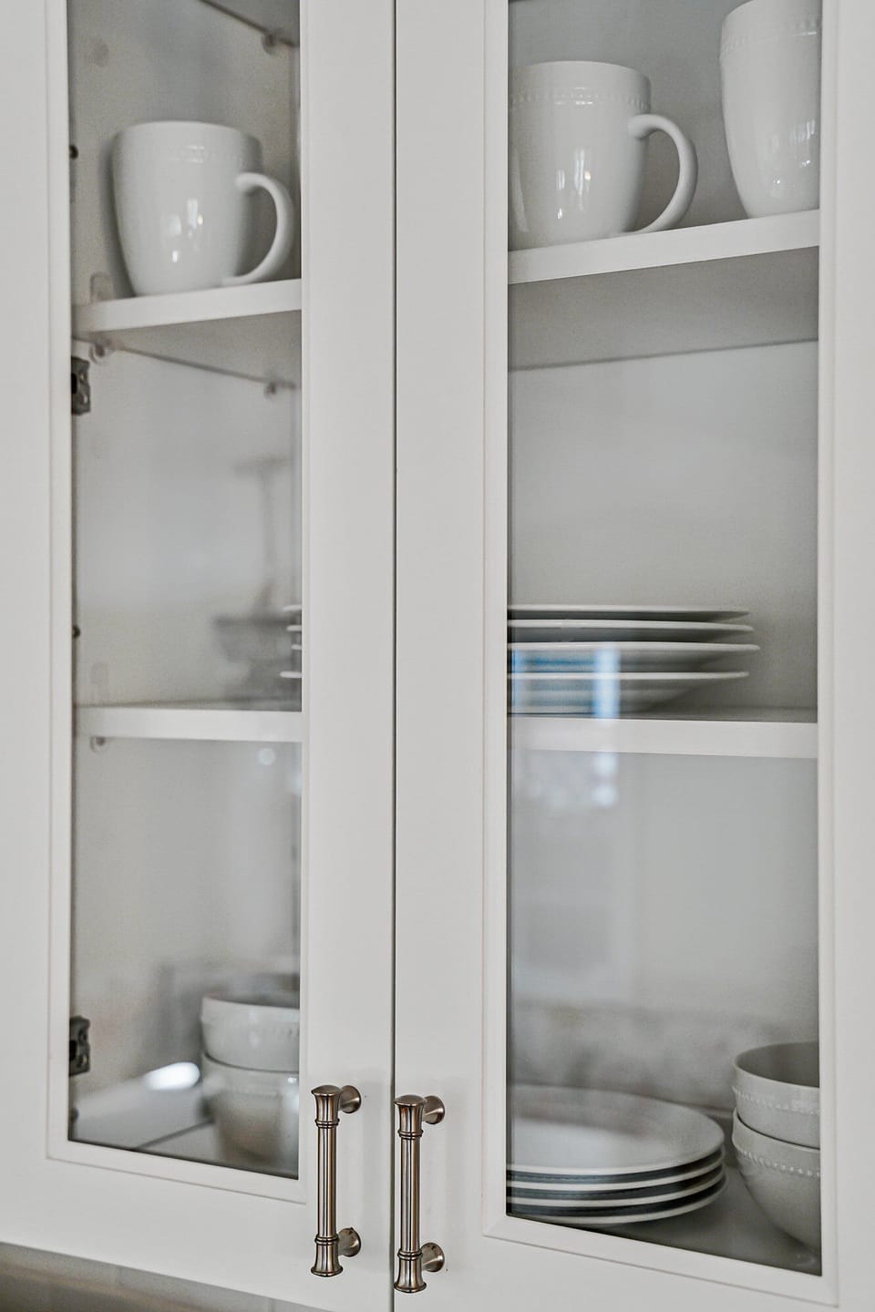 Glass-front cabinets with white dishes and mugs.