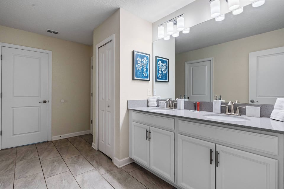 Experience a bright, stylish bathroom with a spacious vanity and sleek white cabinetry. The warm glow of the light fixtures enhances the calming beige walls and modern decor, ensuring your daily routines are a true pleasure.