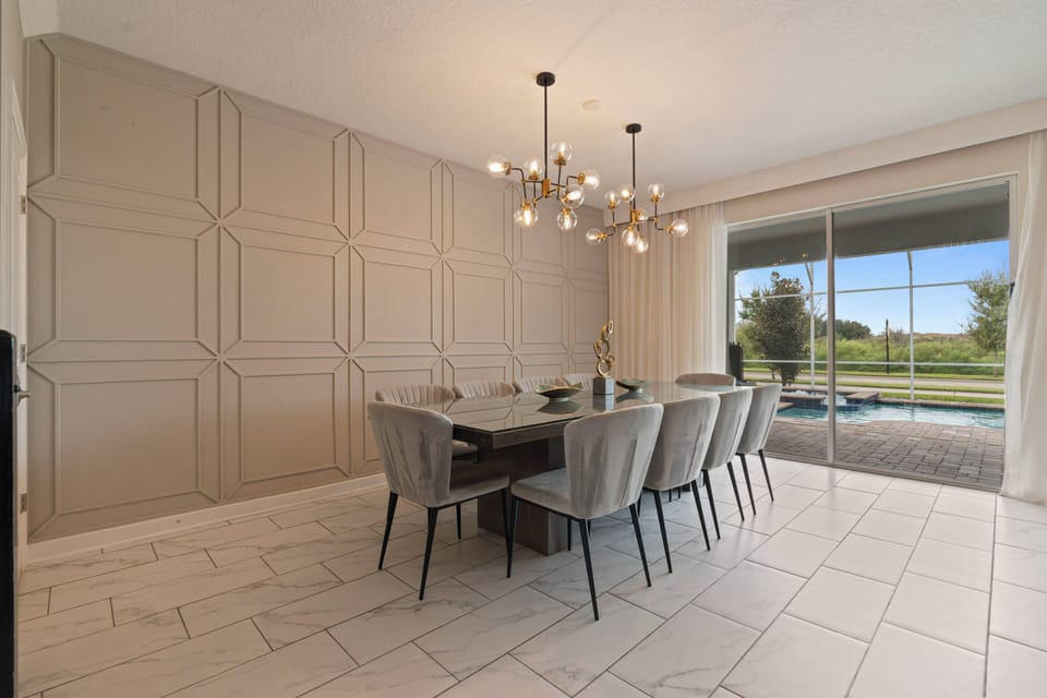 Enjoy dining in a beautifully designed space with a stunning chandelier over a spacious table and plush light gray chairs. Large sliding doors let in natural light and offer views of the pool, creating an inviting atmosphere.