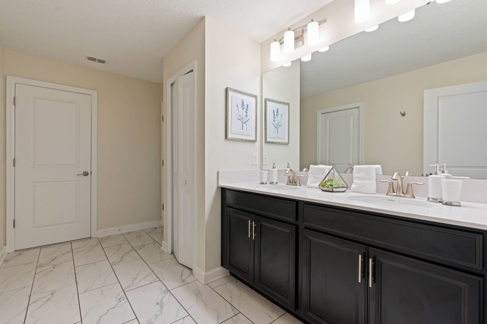 Experience this beautifully designed bathroom with sleek dark cabinetry and light marble flooring. The abundant natural light enhances the chic decor, offering a bright and refreshing atmosphere for your stay.