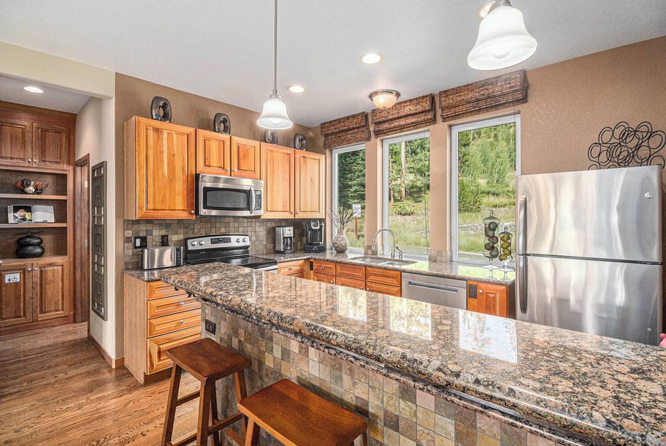 - Fully equipped kitchen with granite countertops and stainless steel appliances
- Tall windows bring in natural light and views of beautiful greenery just outside
- Breakfast bar with stools is perfect for quick meals, coffee, or conversation