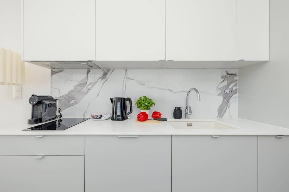 A modern kitchenette with sleek white cabinets and marble-style countertops. Fully equipped for preparing home-cooked meals.