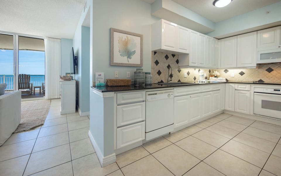 This kitchen features a spacious design with white cabinetry and a view of the beachfront from the adjacent living area