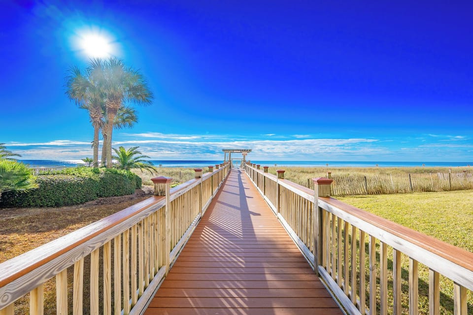 Stroll down the wooden walkway surrounded by lush greenery, leading you directly to the stunning beach and white sands