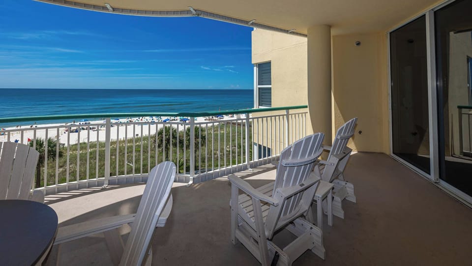 Enjoy a scenic beachfront view from the spacious balcony, featuring comfortable white Adirondack chairs for relaxation