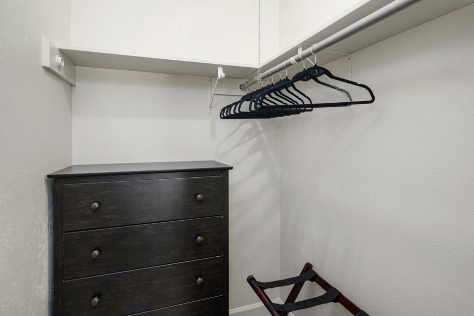 The second bedroom features a spacious walk-in closet equipped with a dresser, hangers, laundry hamper, and a convenient luggage rack for optimal storage and organization.