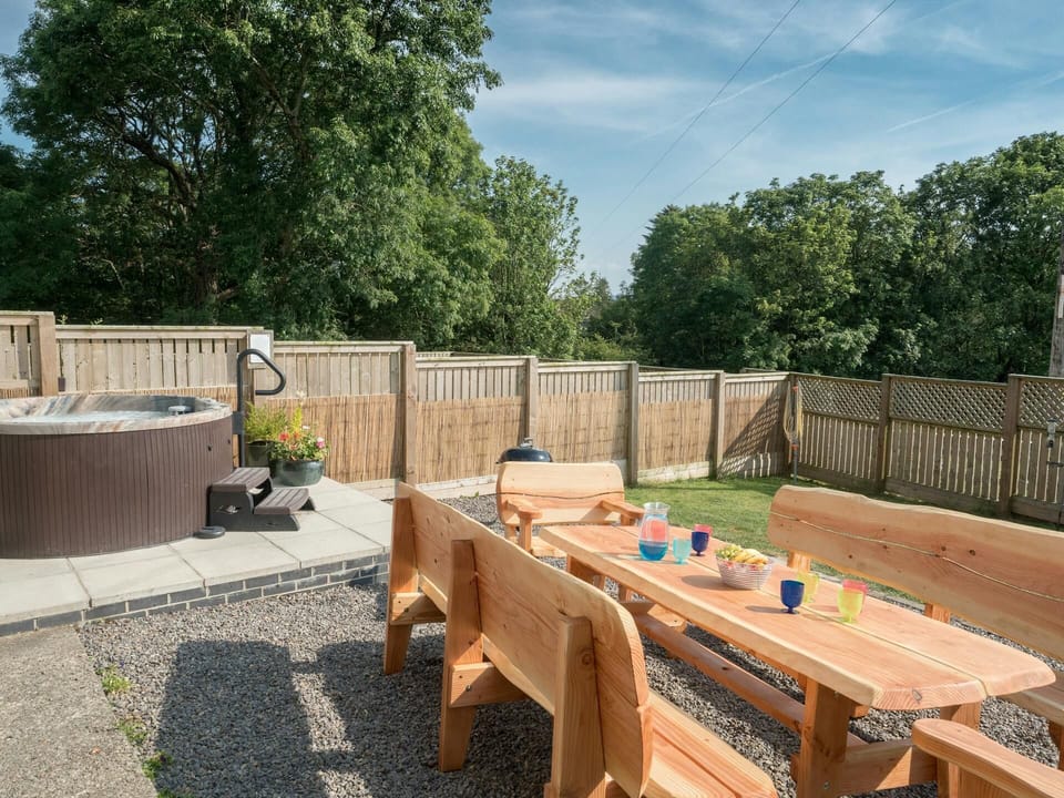Wooden table with benches and chairs, hot tub in fenced garden