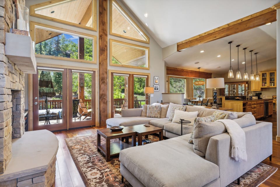 - Bright living room with stone fireplace and large sectional sofa  
- Floor-to-ceiling windows fill space with mountain light and views  
- Easy walkout to deck for hot tub, outdoor seating, and fresh air