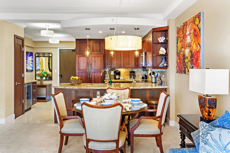 Inviting dining space with a round table, upholstered seating, and island-inspired décor, seamlessly connected to a well-appointed kitchen with rich wood cabinetry and granite countertops creating a polished and welcoming setting for entertaining.