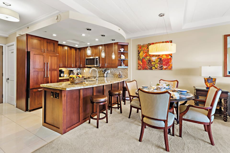 Elegant kitchen and dining area featuring rich wood cabinetry, granite countertops, and a spacious island with bar seating—beautifully complemented by a stylish dining set and island-inspired accents.