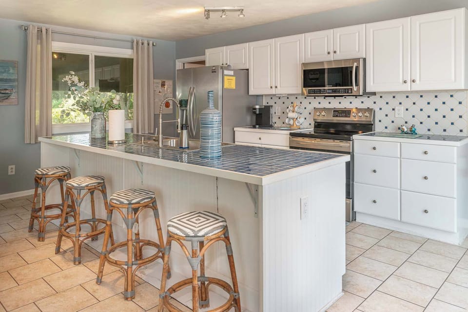Stunning updated kitchen with large island and peninsula countertop, bar seating, stainless steel appliances, modern cabinetry, tile backsplash, and ample prep space