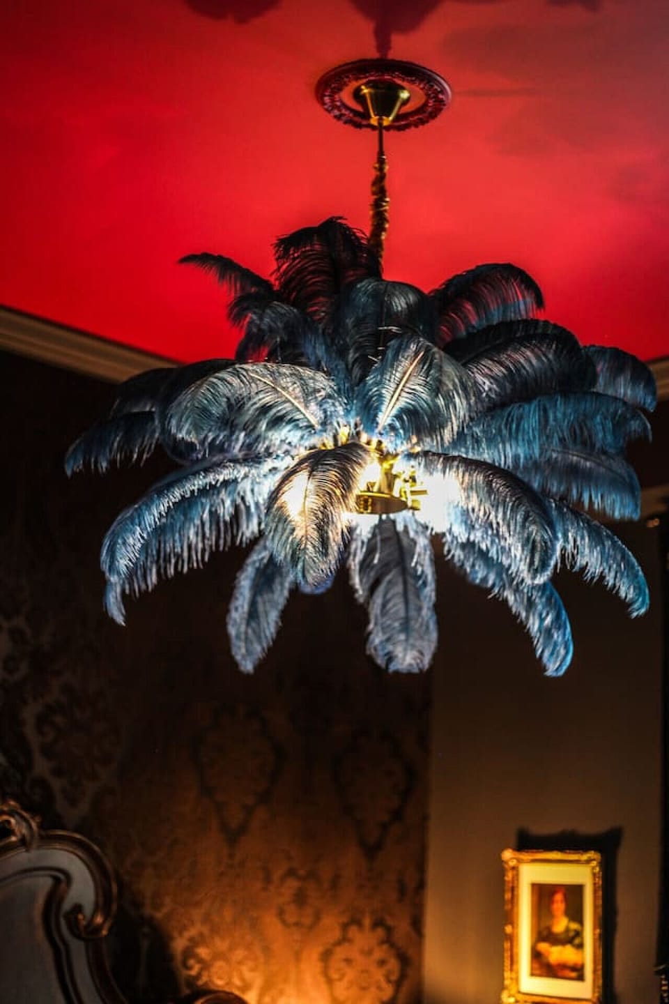 Relax in an opulent bedroom with a King bed, ornate headboard, patterned wallpaper, and a striking blue feathered light fixture.
