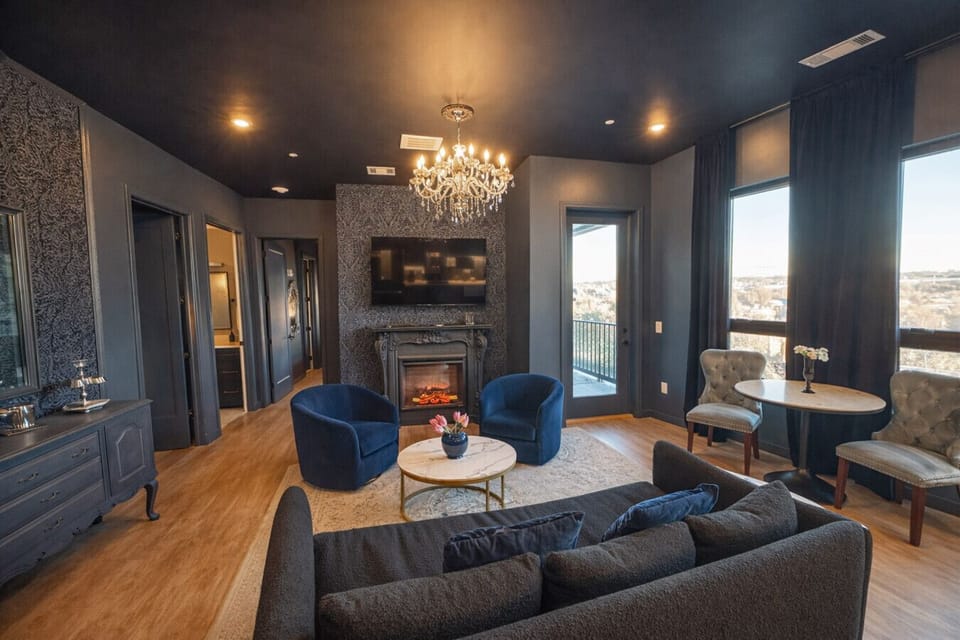 Enjoy a modern, open-plan living space with vibrant blue furniture, a sofa bed, and a stylish kitchen with stainless steel appliances and pendant lighting. A chandelier adds elegance to the cohesive design.