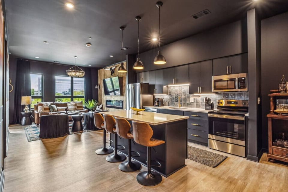 Modern and stylish open-concept kitchen and living area. The kitchen features dark cabinets, a sleek white countertop, and contemporary bar stools.