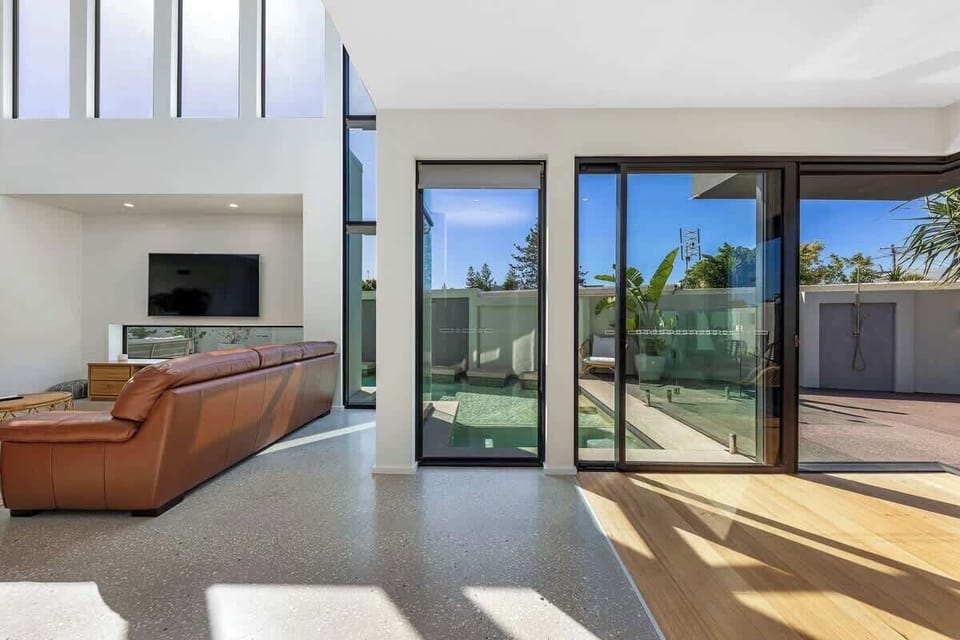 Spacious living area offers a comfortable leather sofa, large windows that let in natural light, and seamless access to an outdoor space with a pool, making it an ideal spot for relaxation.







