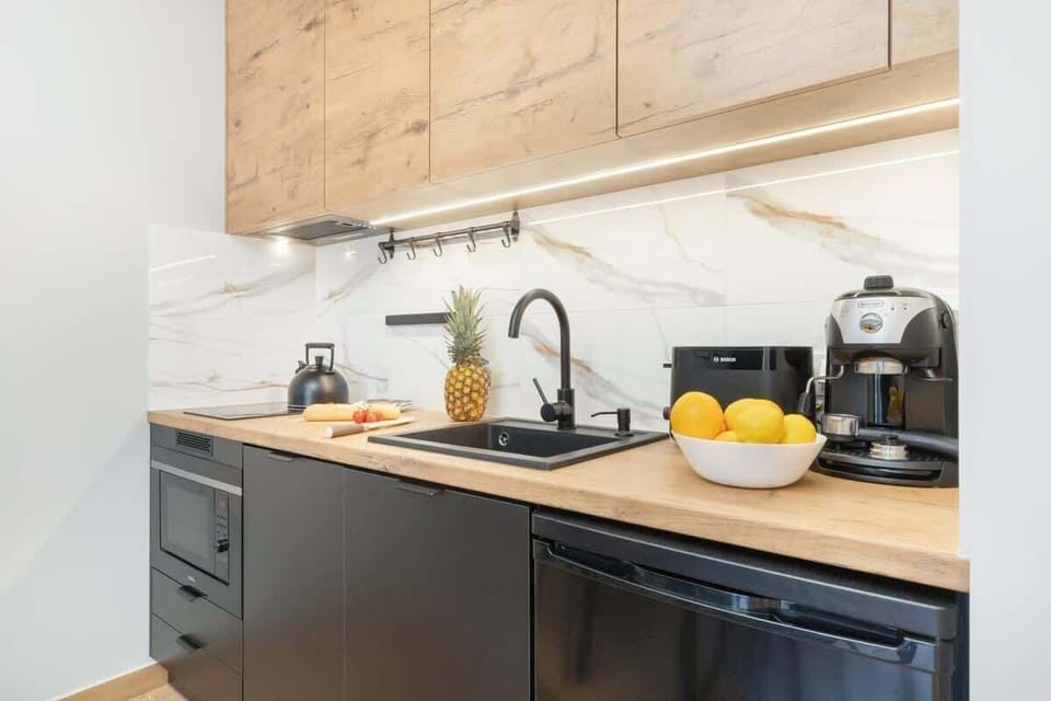 A sleek kitchen with wood cabinets and a black countertop. A kettle and fruit bowl add functionality and charm.