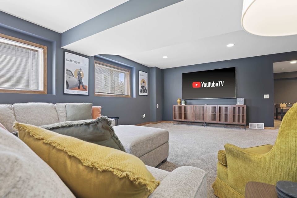 Lower level game room with large sectional sofa, 80" smart TV, arcade game, foosball, and kids play room.