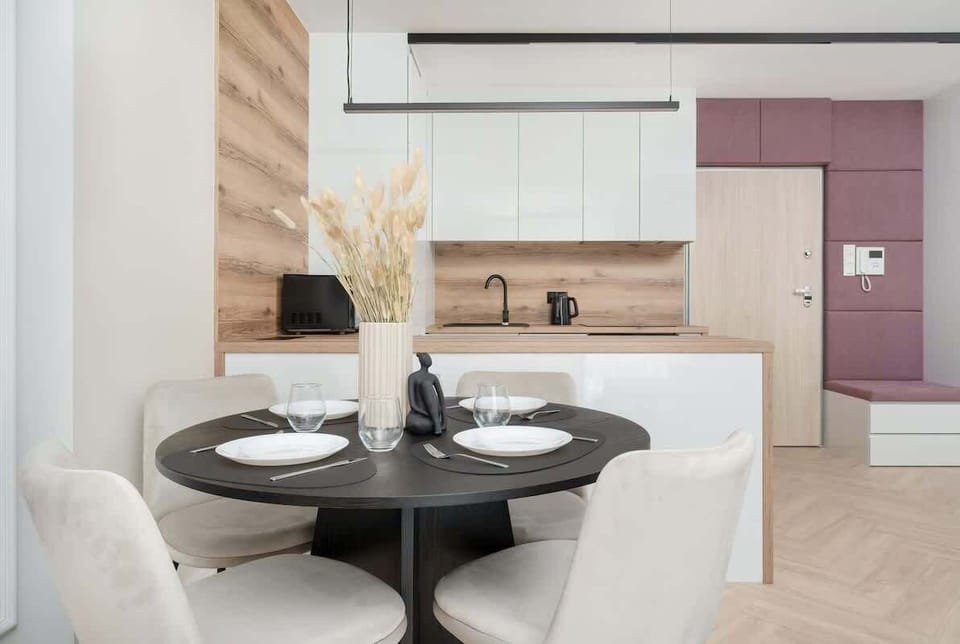A compact dining area with a black round table set for four. The open kitchen in the background adds convenience to the layout.