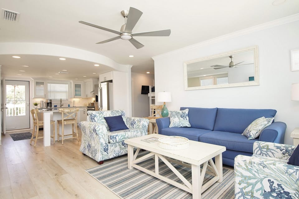 Sink into your coastal-themed living room where blue sofas and botanical patterns create a breezy retreat, perfectly connected to your bright kitchen.