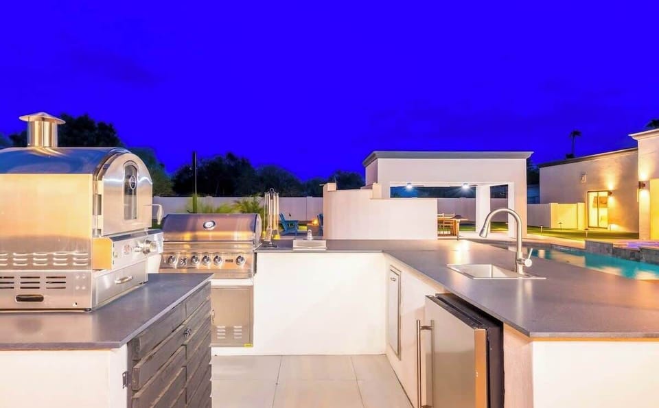 Modern outdoor kitchen with premium grill and sleek countertops, perfect for entertaining under the evening sky while enjoying the illuminated pool and spacious patio beyond.