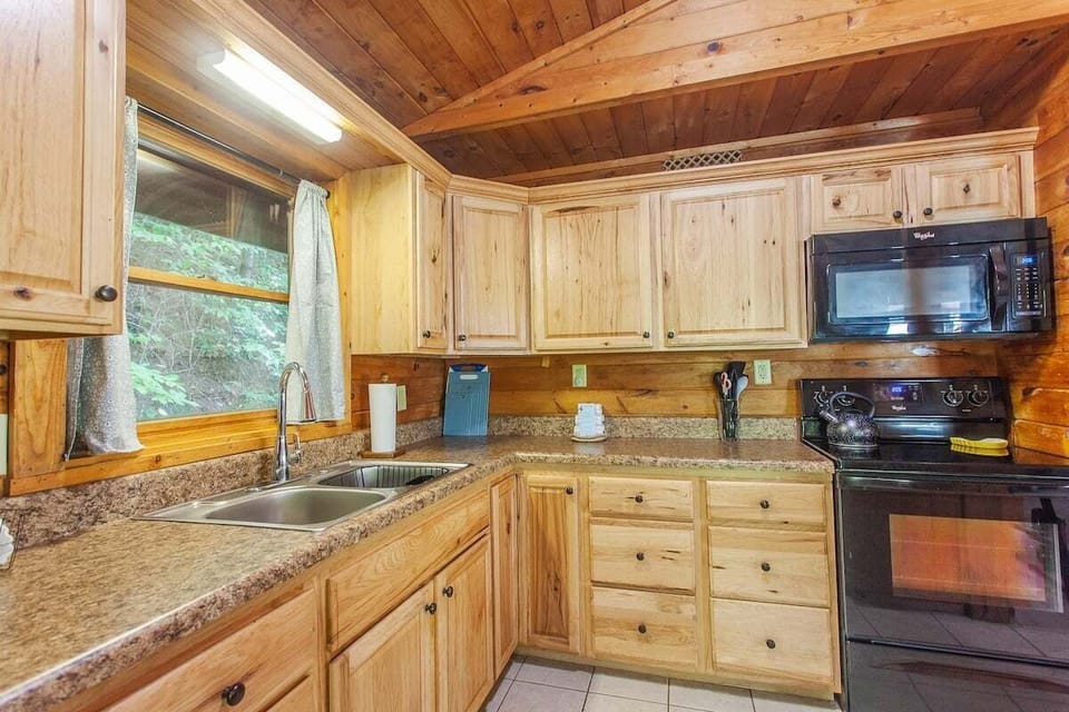 Kitchen workspace with double sink, wood cabinetry, and black appliances beneath vaulted wood ceilings. The functional layout offers ample room for meal preparation.