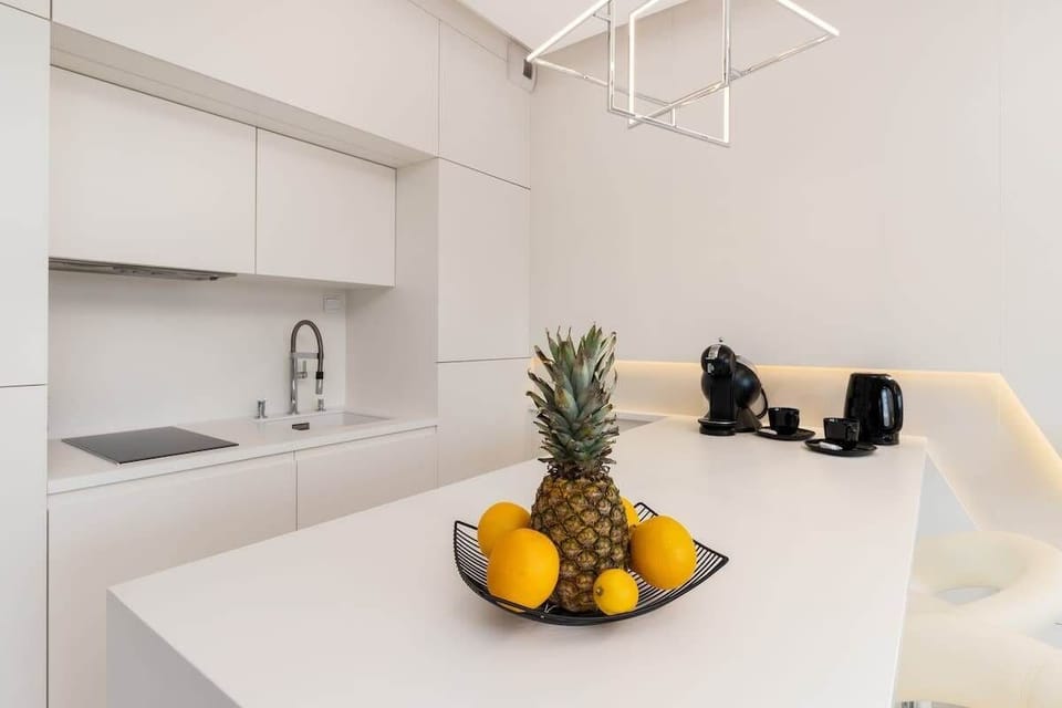 A modern white kitchen with a fruit bowl centerpiece. Bright lighting and clean lines make it welcoming.