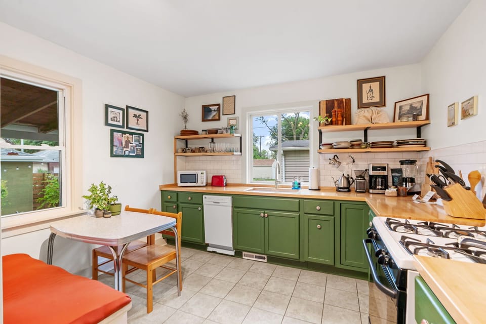 Whip up delicious meals in this charming green kitchen with modern appliances, butcher block counters, and cozy dining nook for morning coffee.