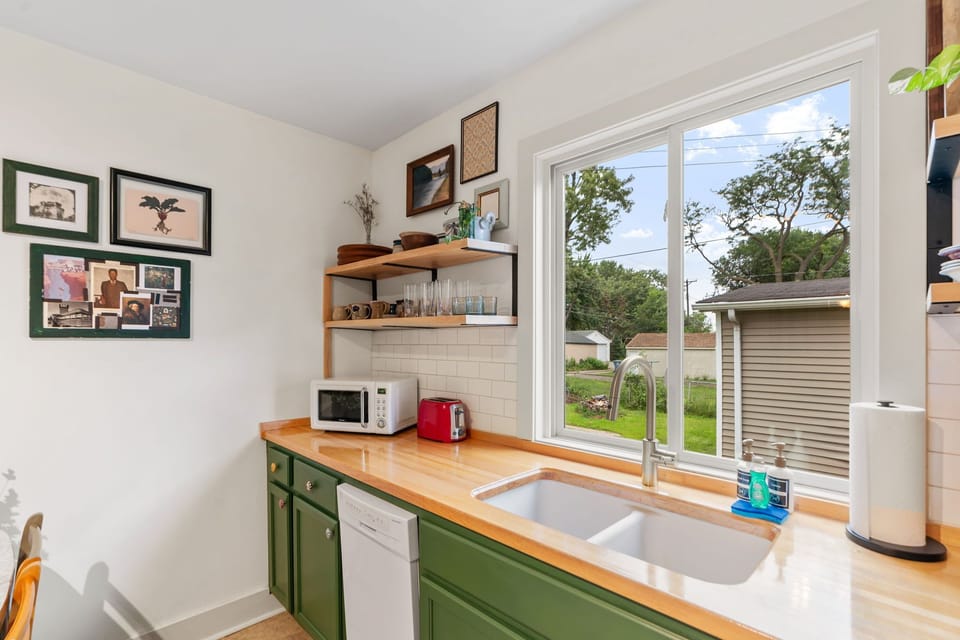 Your fully equipped kitchen features butcher block counters, charming green cabinets, and a bright window overlooking the peaceful neighborhood.