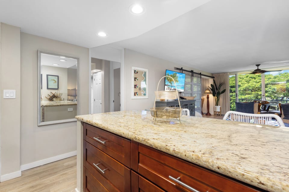 Your spacious kitchen features gleaming granite countertops and rich wood cabinetry, perfect for preparing tropical-inspired meals while enjoying lush garden views through expansive windows.