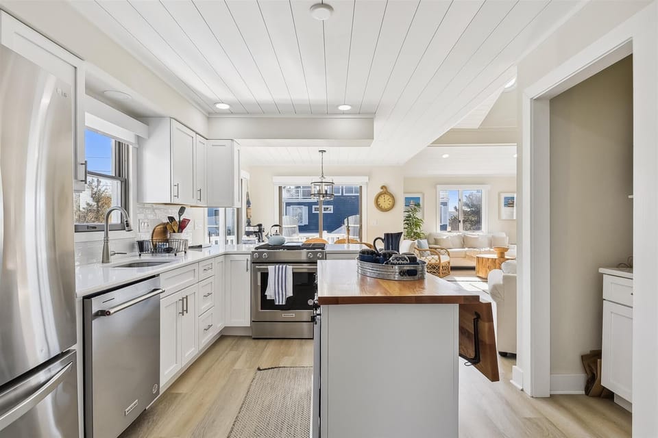 Your bright, airy kitchen beckons with gleaming white cabinets, stainless appliances, and a warm wood island—perfect for preparing meals while chatting with loved ones in the sunny living space beyond.