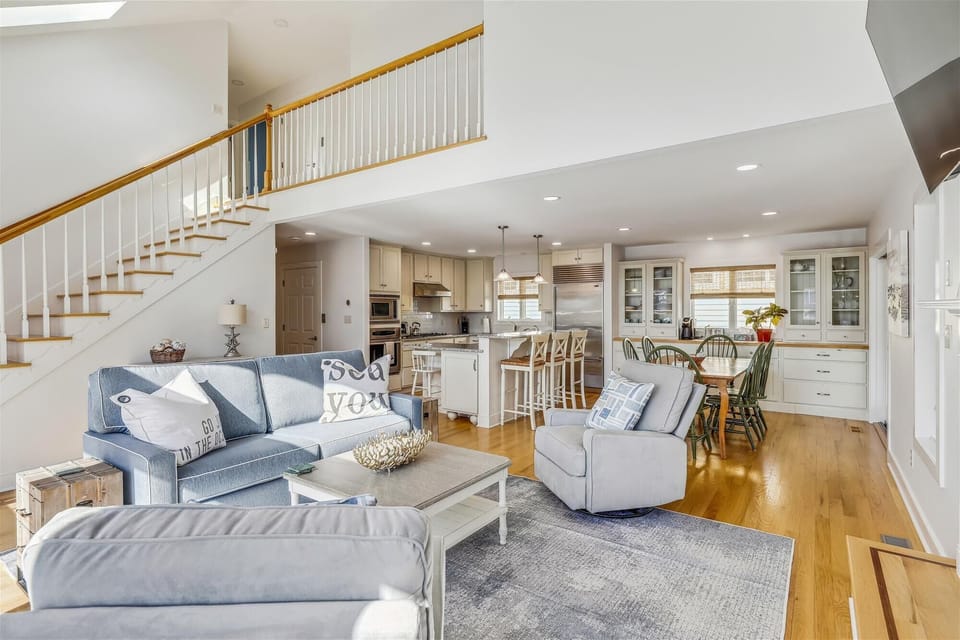 Your sunlit coastal retreat features an open living area with soaring ceilings, a gourmet kitchen with granite counters, and cozy seating that flows seamlessly from lounge to dining—perfect for gathering with loved ones.