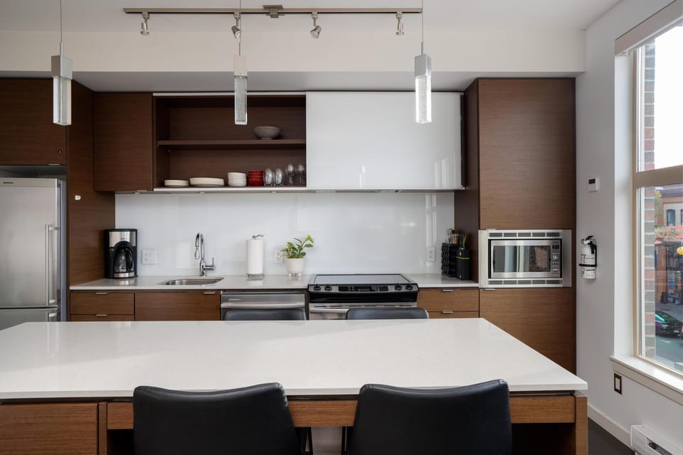 Gather around the expansive kitchen island, offering ample prep space and stylish dark-leather barstool seating for your meals.