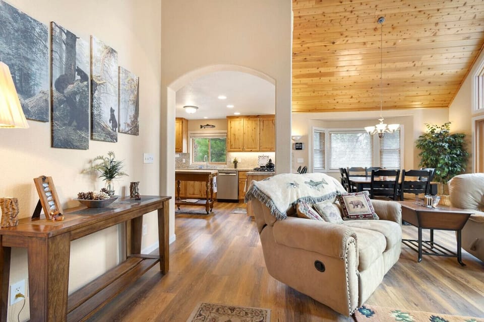 Seamless flow from cozy living area to spacious kitchen and dining space, with wood accents, vaulted ceilings, and forest views — perfect for mountain living or vacation comfort.